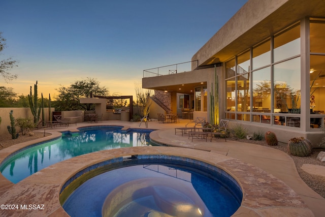 pool at dusk with a patio area, exterior kitchen, and an in ground hot tub