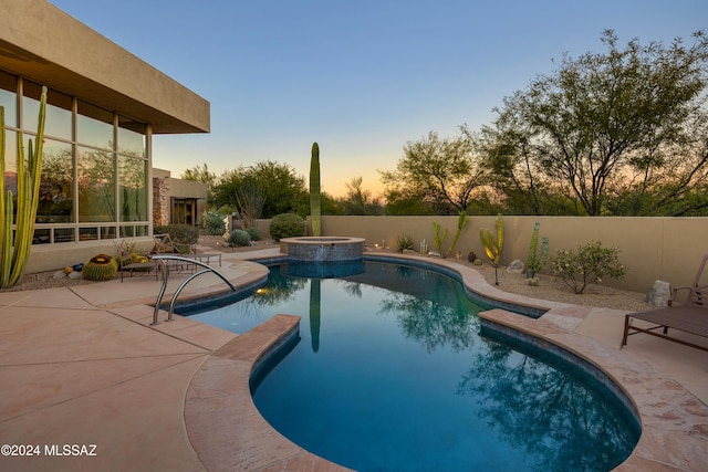 pool at dusk featuring a patio area and an in ground hot tub