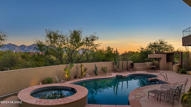 pool at dusk with a mountain view, a patio area, an in ground hot tub, and exterior kitchen