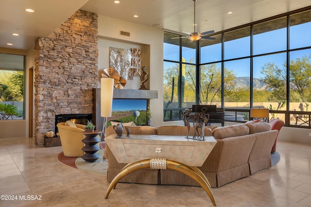 living room with ceiling fan, a stone fireplace, a towering ceiling, and a mountain view