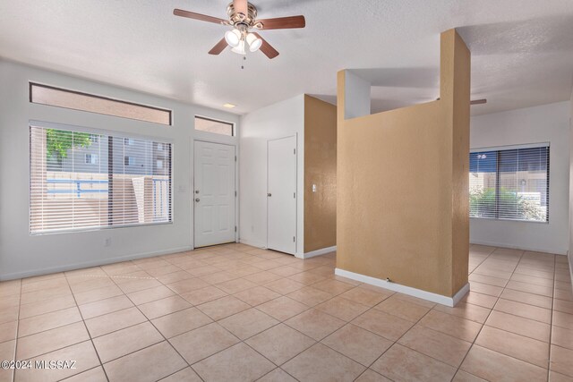 empty room featuring a textured ceiling, light tile patterned flooring, ceiling fan, and plenty of natural light