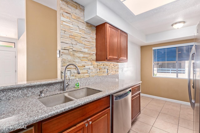 kitchen featuring a textured ceiling, stainless steel dishwasher, sink, and light stone counters