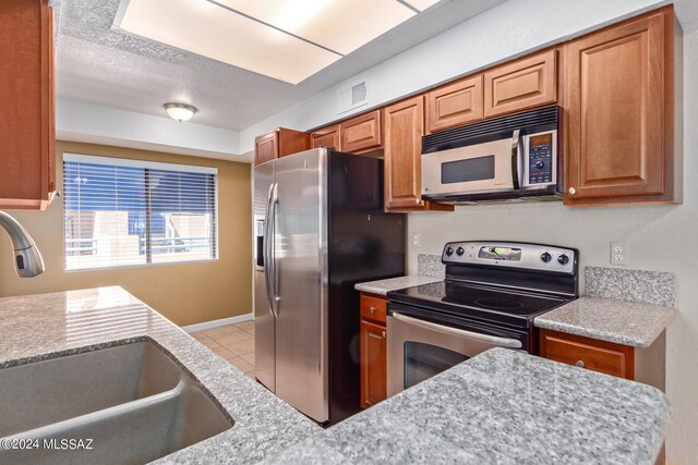 kitchen featuring light stone counters, light tile patterned flooring, sink, a textured ceiling, and stainless steel appliances