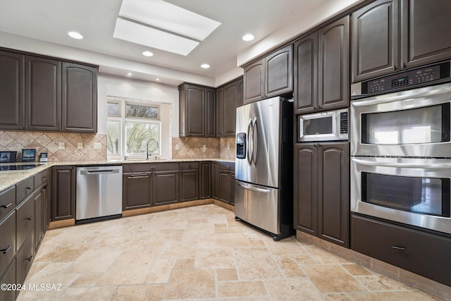 kitchen with sink, light stone counters, a skylight, stainless steel appliances, and backsplash