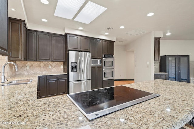 kitchen featuring sink, a skylight, stainless steel appliances, dark brown cabinetry, and decorative backsplash