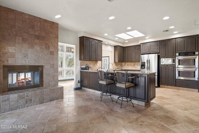 kitchen featuring sink, appliances with stainless steel finishes, light stone countertops, decorative backsplash, and kitchen peninsula