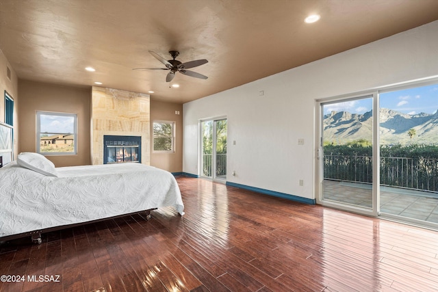 bedroom featuring hardwood / wood-style floors, a large fireplace, access to exterior, ceiling fan, and a mountain view