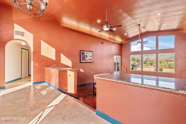 kitchen with hanging light fixtures, ceiling fan with notable chandelier, light stone countertops, and high vaulted ceiling