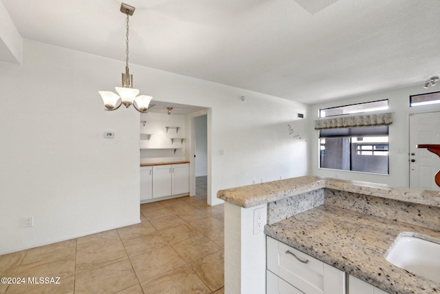 kitchen with white cabinets, hanging light fixtures, light stone counters, and a notable chandelier