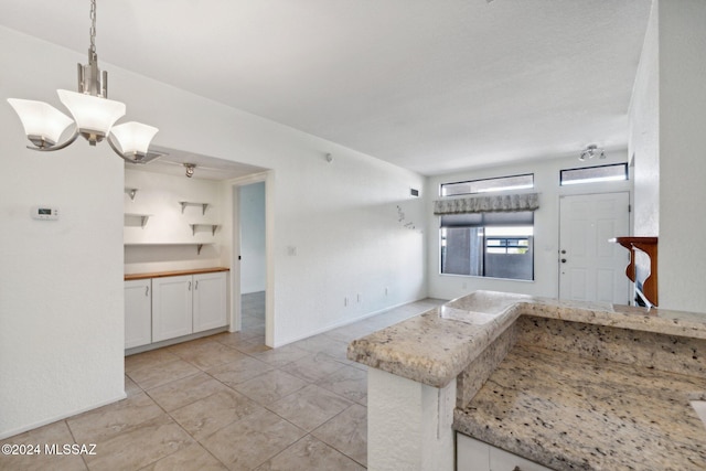 kitchen with light stone counters, white cabinetry, hanging light fixtures, an inviting chandelier, and kitchen peninsula