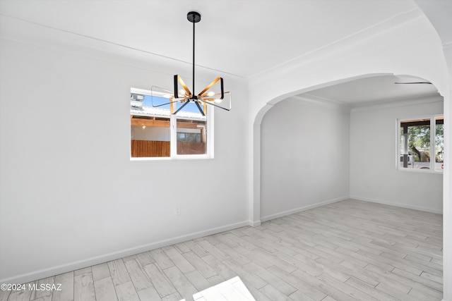 spare room with light wood-type flooring, ornamental molding, and a chandelier