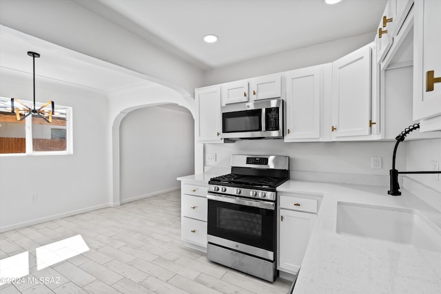 kitchen featuring stainless steel appliances, sink, light hardwood / wood-style floors, white cabinetry, and hanging light fixtures