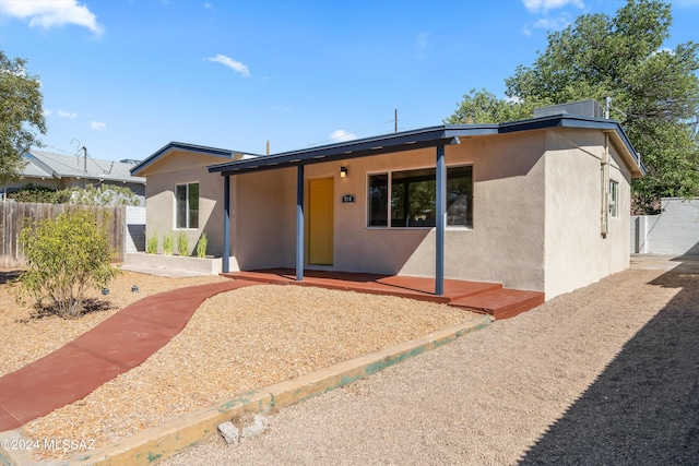 view of front facade with a porch, stucco siding, and fence