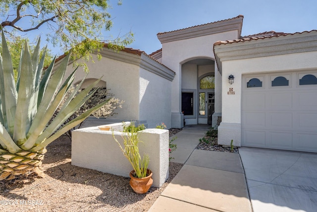 entrance to property with stucco siding, a tile roof, and a garage