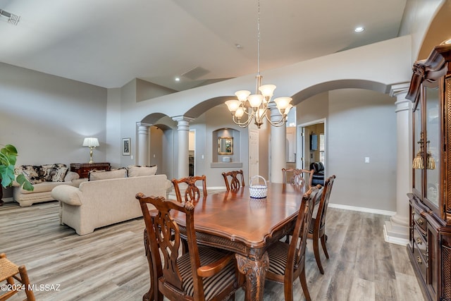 dining area featuring light wood finished floors, arched walkways, a chandelier, and ornate columns