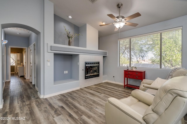 living room featuring wood finished floors, arched walkways, a fireplace, baseboards, and ceiling fan