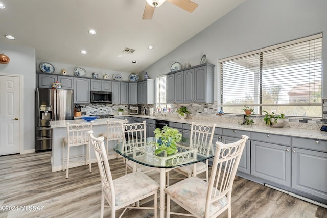 kitchen featuring sink, appliances with stainless steel finishes, wood-type flooring, a kitchen island, and vaulted ceiling