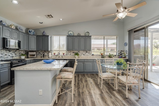 kitchen featuring gray cabinets, vaulted ceiling, a center island, gas range, and plenty of natural light