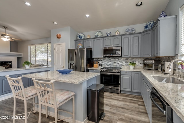 kitchen featuring sink, appliances with stainless steel finishes, a kitchen breakfast bar, a center island, and light stone countertops