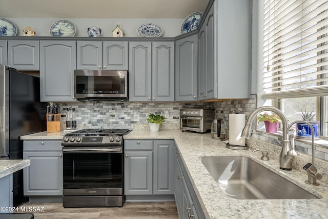 kitchen featuring sink, gray cabinetry, stainless steel appliances, light stone countertops, and decorative backsplash