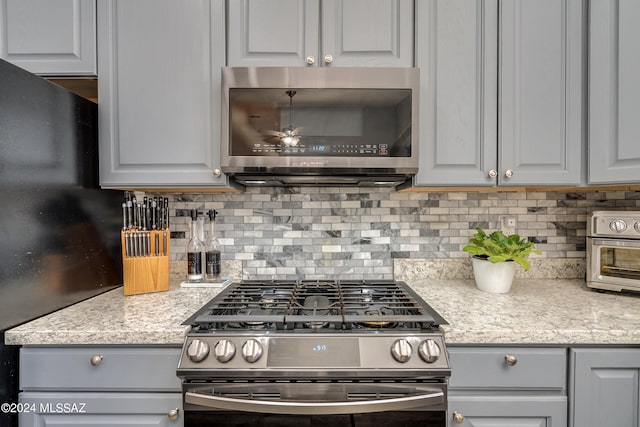 kitchen featuring stainless steel appliances, gray cabinets, and light stone counters