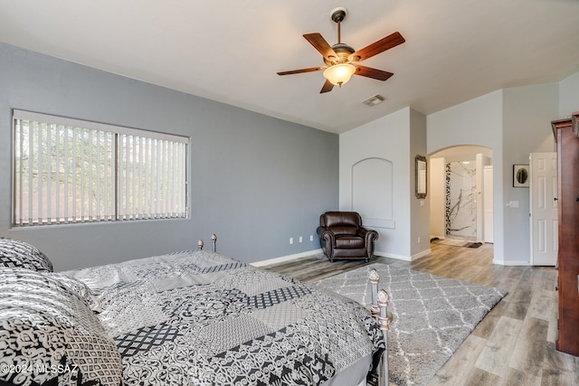 bedroom with arched walkways, visible vents, baseboards, and wood finished floors