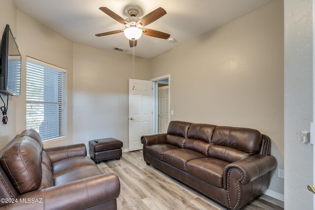 living room with a ceiling fan, visible vents, light wood finished floors, and baseboards