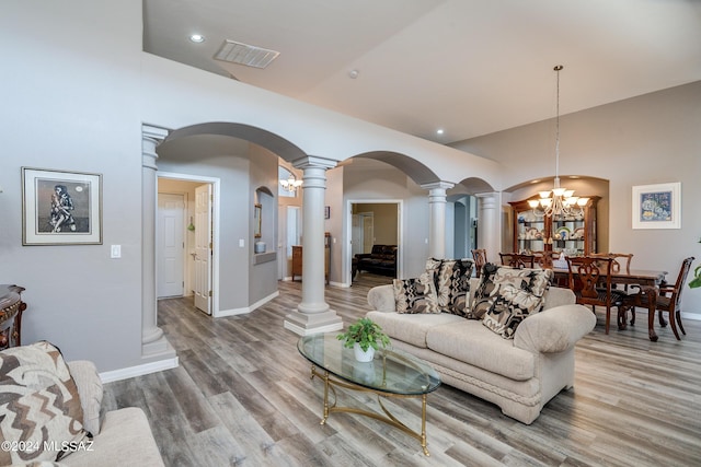 living room with visible vents, light wood-style flooring, arched walkways, a notable chandelier, and ornate columns