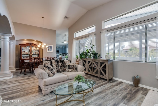 living area featuring baseboards, light wood finished floors, ornate columns, lofted ceiling, and a notable chandelier