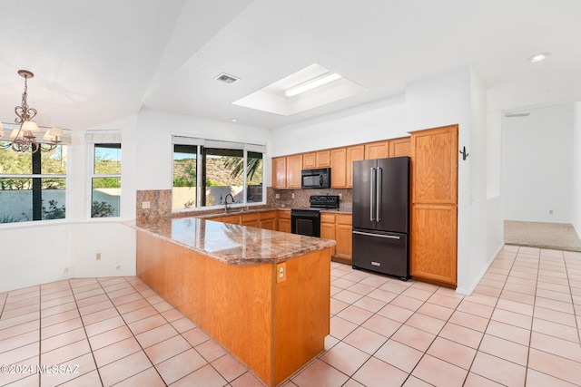 kitchen featuring kitchen peninsula, light tile patterned floors, black appliances, dark stone counters, and a notable chandelier