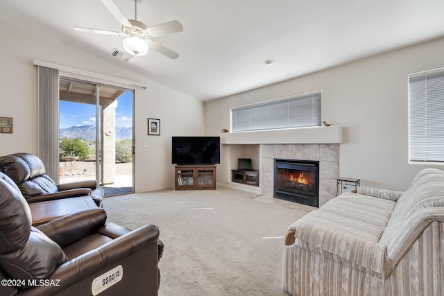 carpeted living room with ceiling fan, a tiled fireplace, and vaulted ceiling