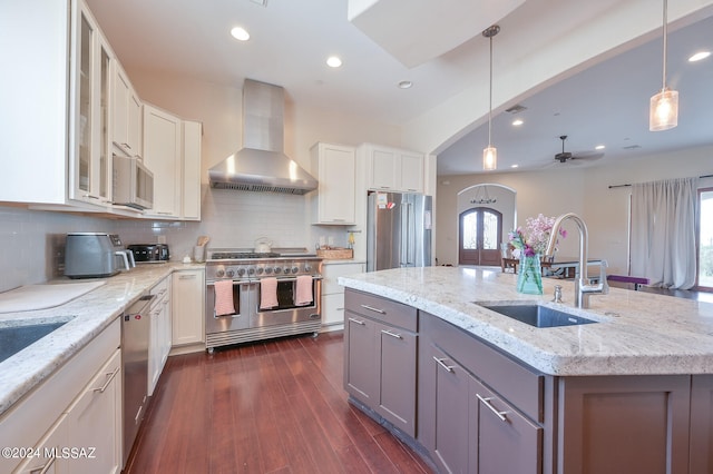 kitchen with high end appliances, white cabinetry, wall chimney range hood, and a wealth of natural light