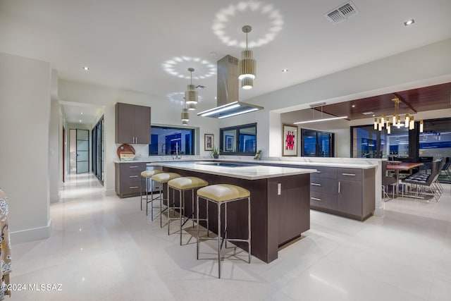 kitchen with dark brown cabinets, kitchen peninsula, a kitchen bar, decorative light fixtures, and a spacious island