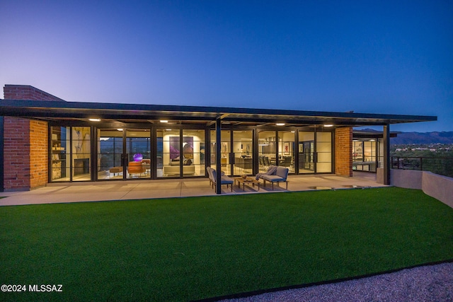 back house at dusk with a patio, a lawn, and ceiling fan