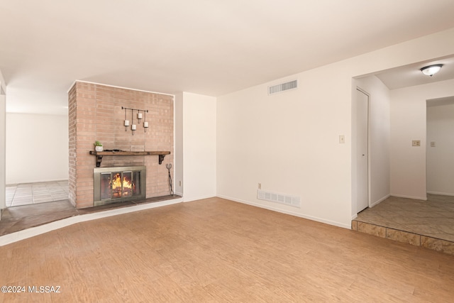 unfurnished living room with wood-type flooring and a brick fireplace