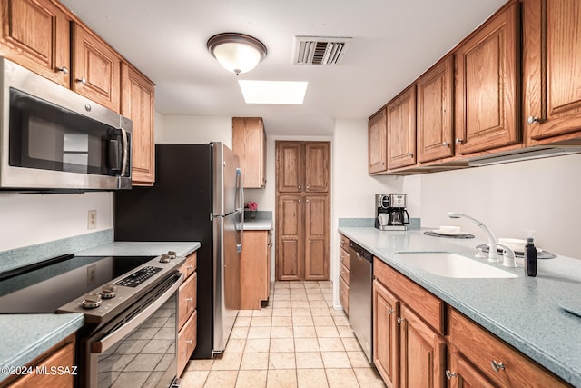 kitchen featuring a skylight, appliances with stainless steel finishes, light tile patterned floors, and sink