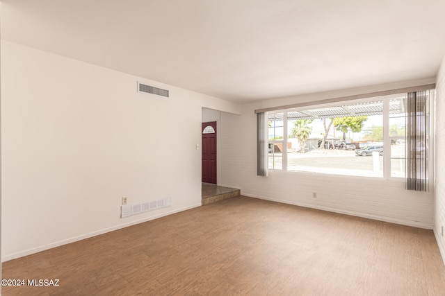 unfurnished room featuring brick wall and hardwood / wood-style floors