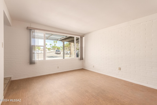 unfurnished room featuring wood-type flooring and brick wall