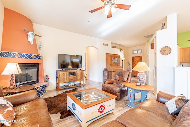 living room featuring a tiled fireplace, light wood-type flooring, and ceiling fan