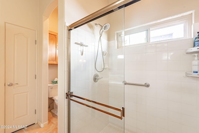 bathroom featuring toilet, tile patterned floors, and a shower with shower door