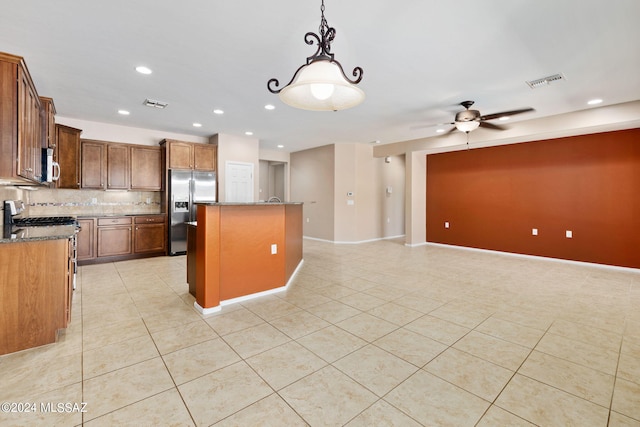 kitchen with ceiling fan, a kitchen island, appliances with stainless steel finishes, dark stone countertops, and decorative backsplash