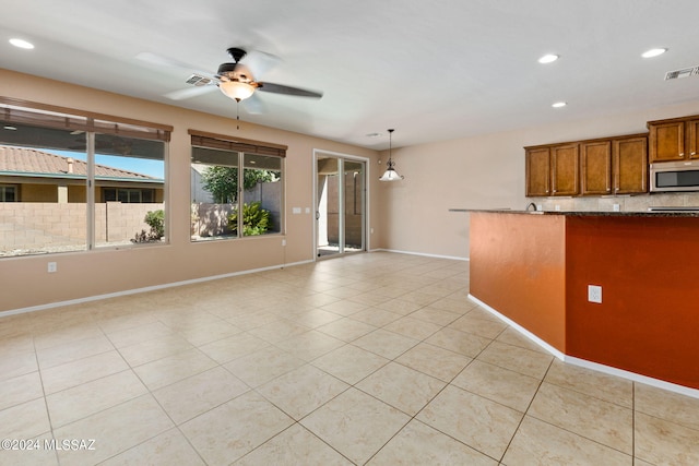 kitchen with hanging light fixtures, decorative backsplash, light tile patterned floors, ceiling fan, and stone countertops