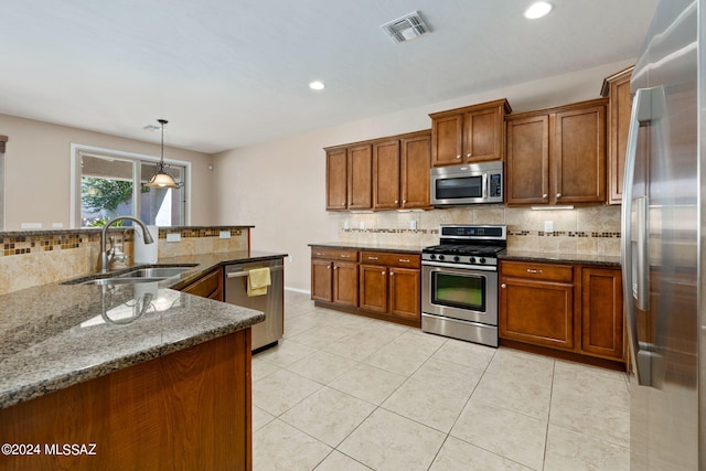 kitchen with pendant lighting, sink, backsplash, stainless steel appliances, and dark stone countertops