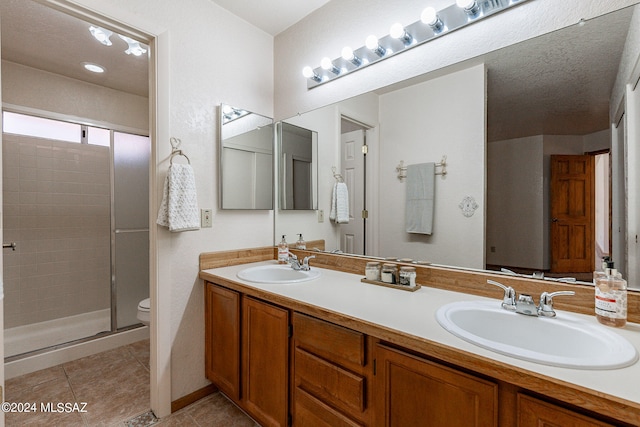 bathroom featuring a shower with shower door, vanity, a textured ceiling, toilet, and tile patterned floors