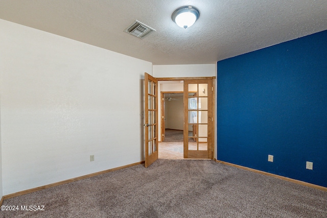 carpeted spare room with a textured ceiling and french doors