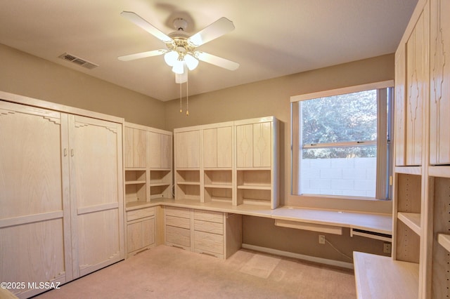 unfurnished office with light carpet, built in desk, and ceiling fan