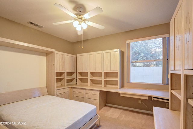 bedroom featuring built in desk, light colored carpet, and ceiling fan