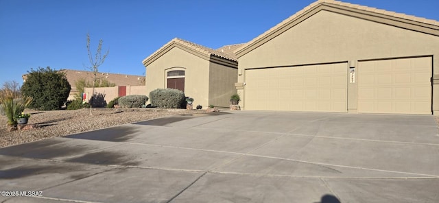 view of front of home with stucco siding, driveway, a tile roof, and a garage