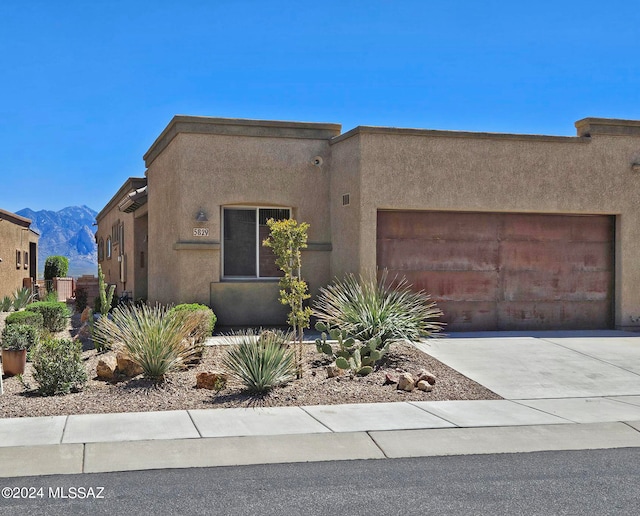 adobe home featuring a garage, concrete driveway, a mountain view, and stucco siding