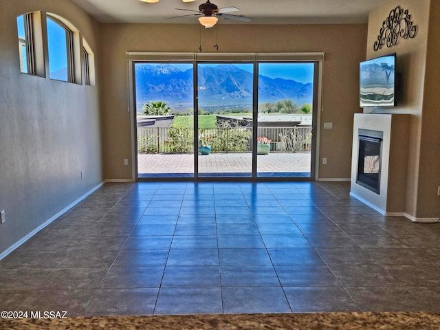 spare room with a glass covered fireplace, dark tile patterned flooring, ceiling fan, and baseboards